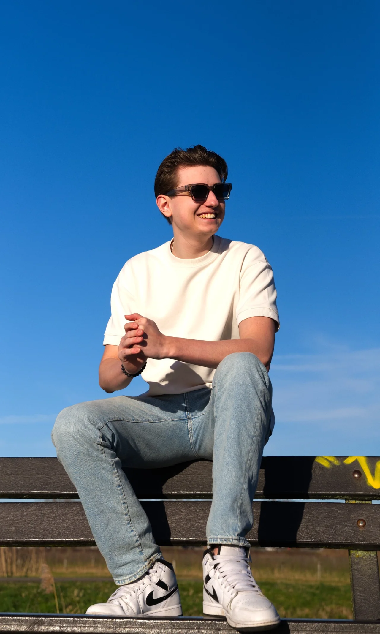 Sebas zit lachend in de zon op een houten trap